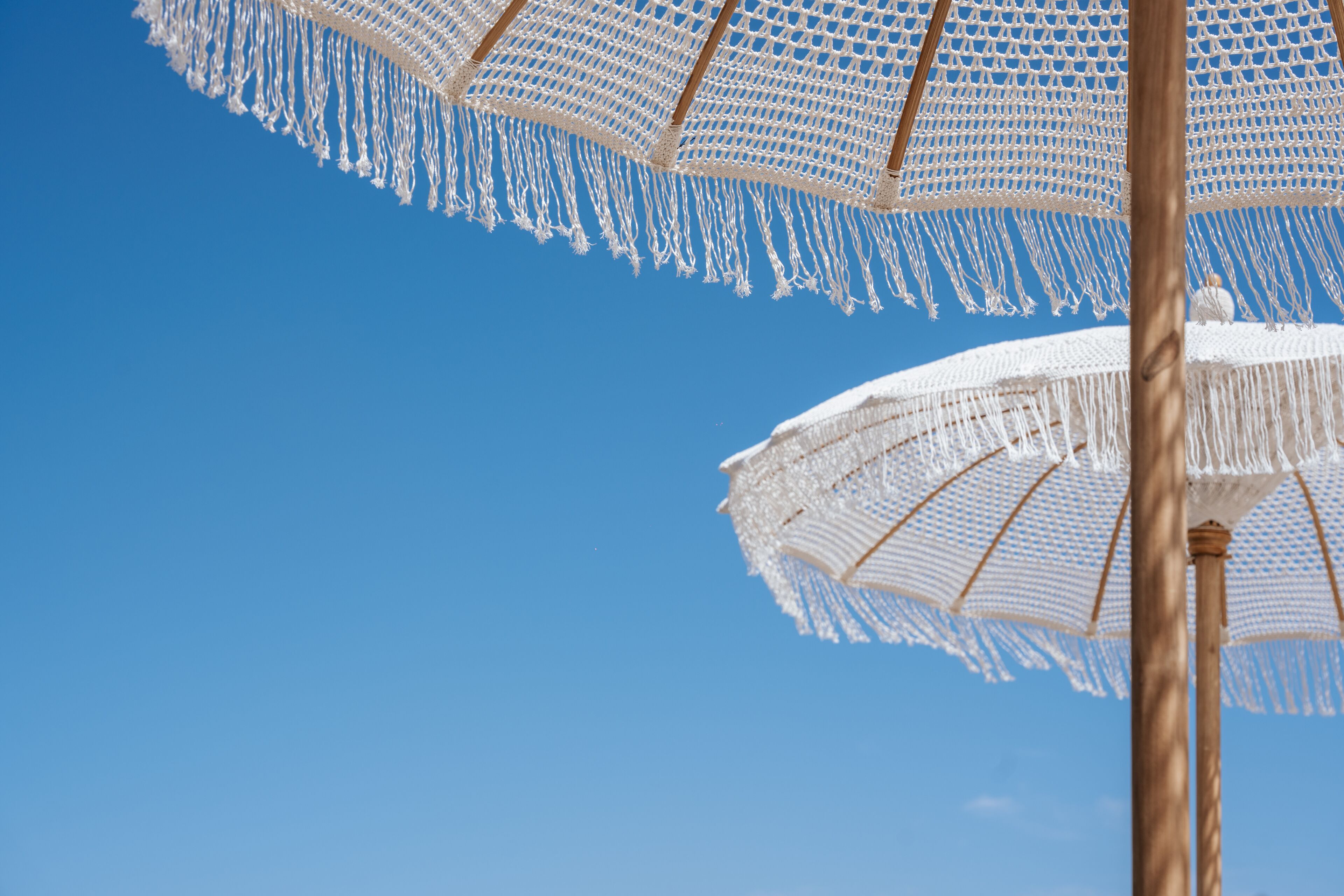 A clear blue sky with two white beach umbrellas.