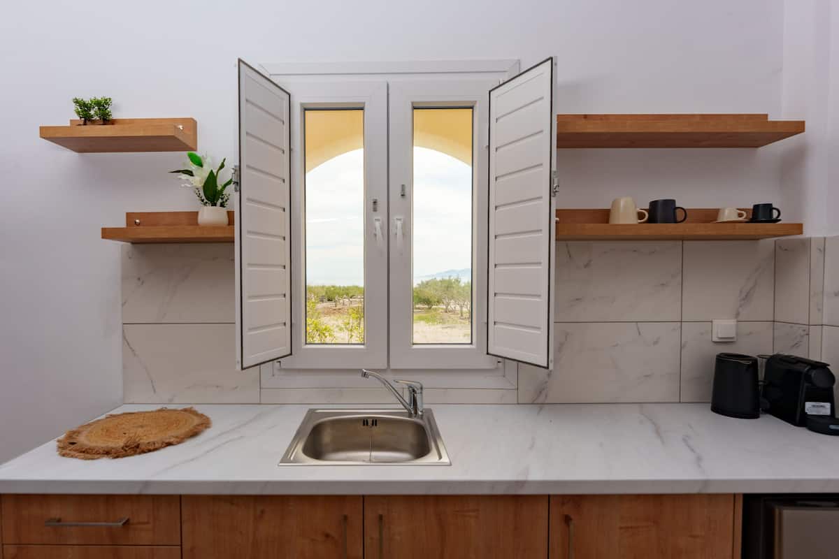 A kitchen with a double door window, wooden shelves, a sink, and a coffee maker.