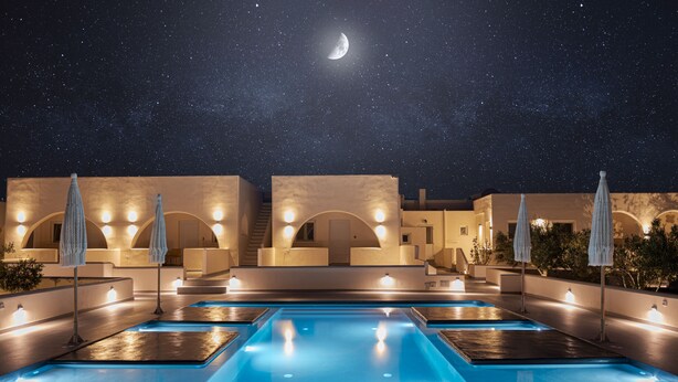 Uma área de piscina à noite, com várias piscinas iluminadas por luzes no teto, e uma lua crescente visível no céu.