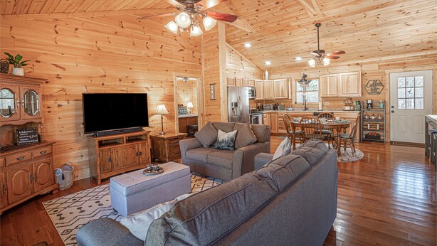 A spacious living room with a large flat-screen TV, a gray sofa, and a wooden ceiling.