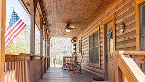 A wooden cabin with a porch, an American flag, rocking chairs, and a door with a mountain sign.