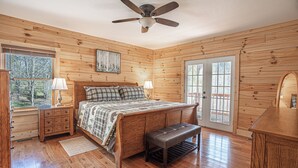 A wooden cabin bedroom with a bed, bench, nightstands, and a ceiling fan.