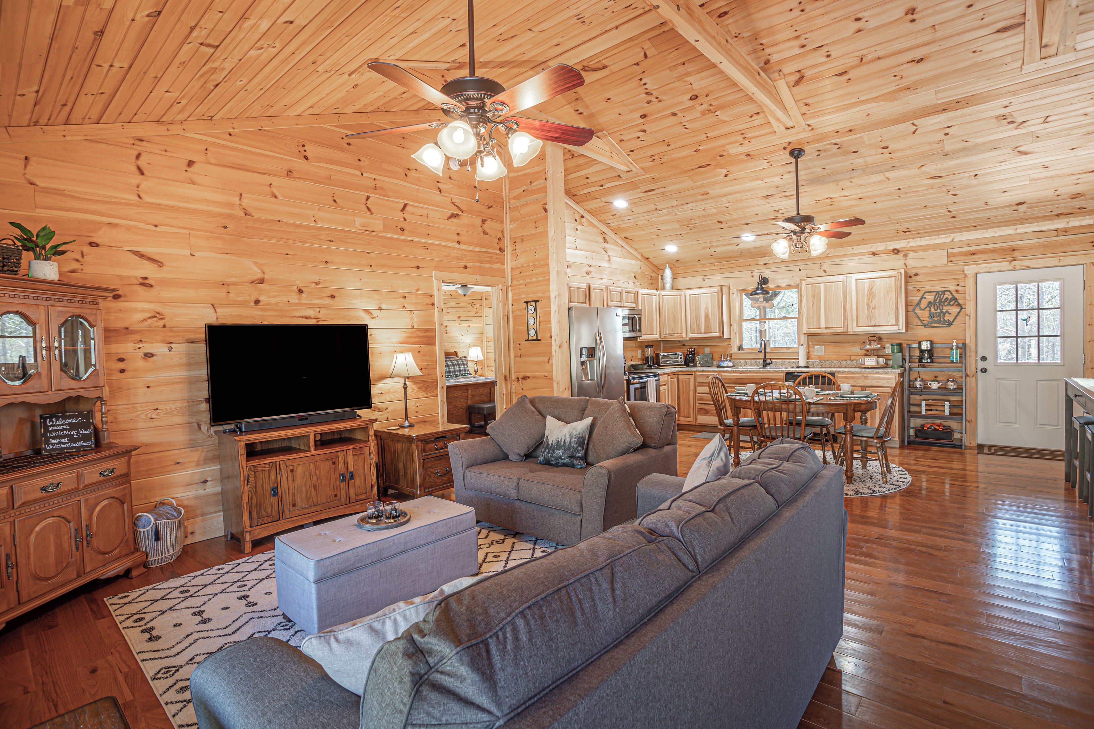 A spacious living room with a large flat-screen TV, a gray sofa, and a wooden ceiling.