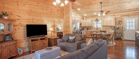 A spacious living room with a large flat-screen TV, a gray sofa, and a wooden ceiling.