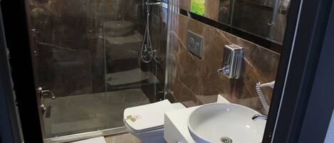 Un baño moderno con cabina de ducha de vidrio, un lavabo blanco y un inodoro.