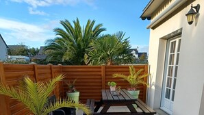 Ein Patio mit Holztisch und Bänken, umgeben von Kübelpflanzen und einem Holzzaun.