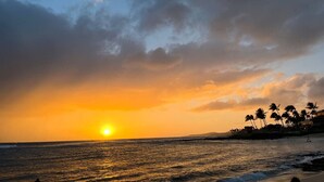 A sunset over a beach with palm trees and a calm sea.