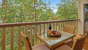 A balcony with wicker chairs, a glass table, and a charcuterie board with cheese, grapes, and meats.