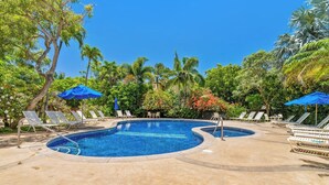 A swimming pool with lounge chairs and umbrellas, surrounded by tropical vegetation.