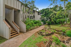 Um edifício com uma escadaria que leva a uma entrada, rodeado por vegetação exuberante e um pequeno riacho.