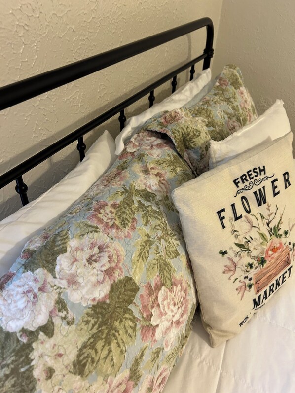 A bed with floral bedding and a pillow with 'Fresh Flower Market' text.