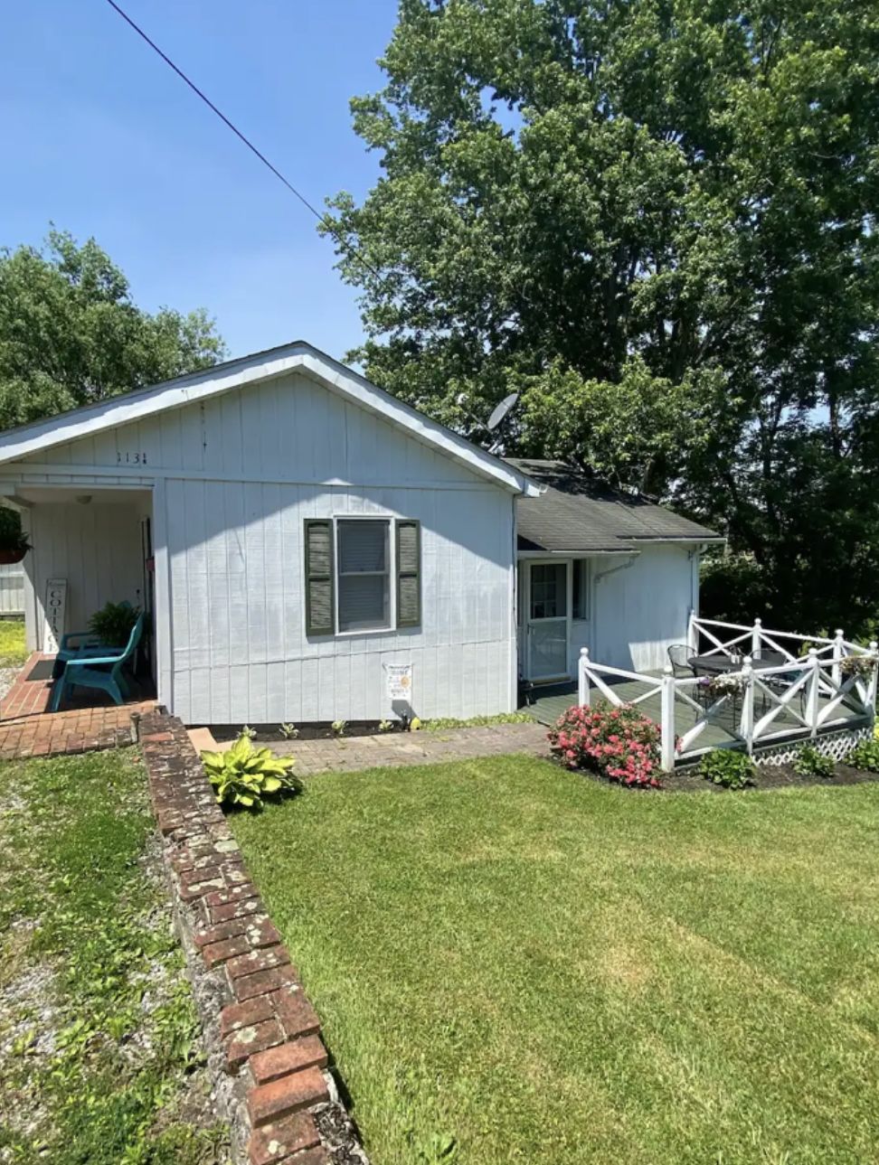 A single-story house with a front porch, a brick pathway leading to the entrance, and a small garden area with a white fence.