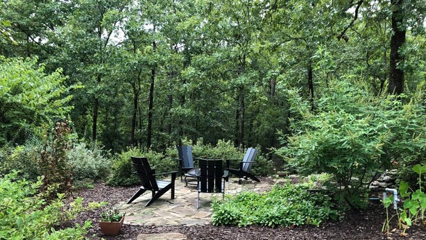 Une terrasse aménagée dans un jardin, avec des chaises Adirondack et une table, le tout entouré d’une végétation luxuriante et d’arbres.