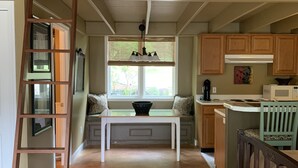 Une cuisine spacieuse avec un plafond haut, une échelle en bois, une table à manger et une vue sur l’extérieur par une fenêtre.