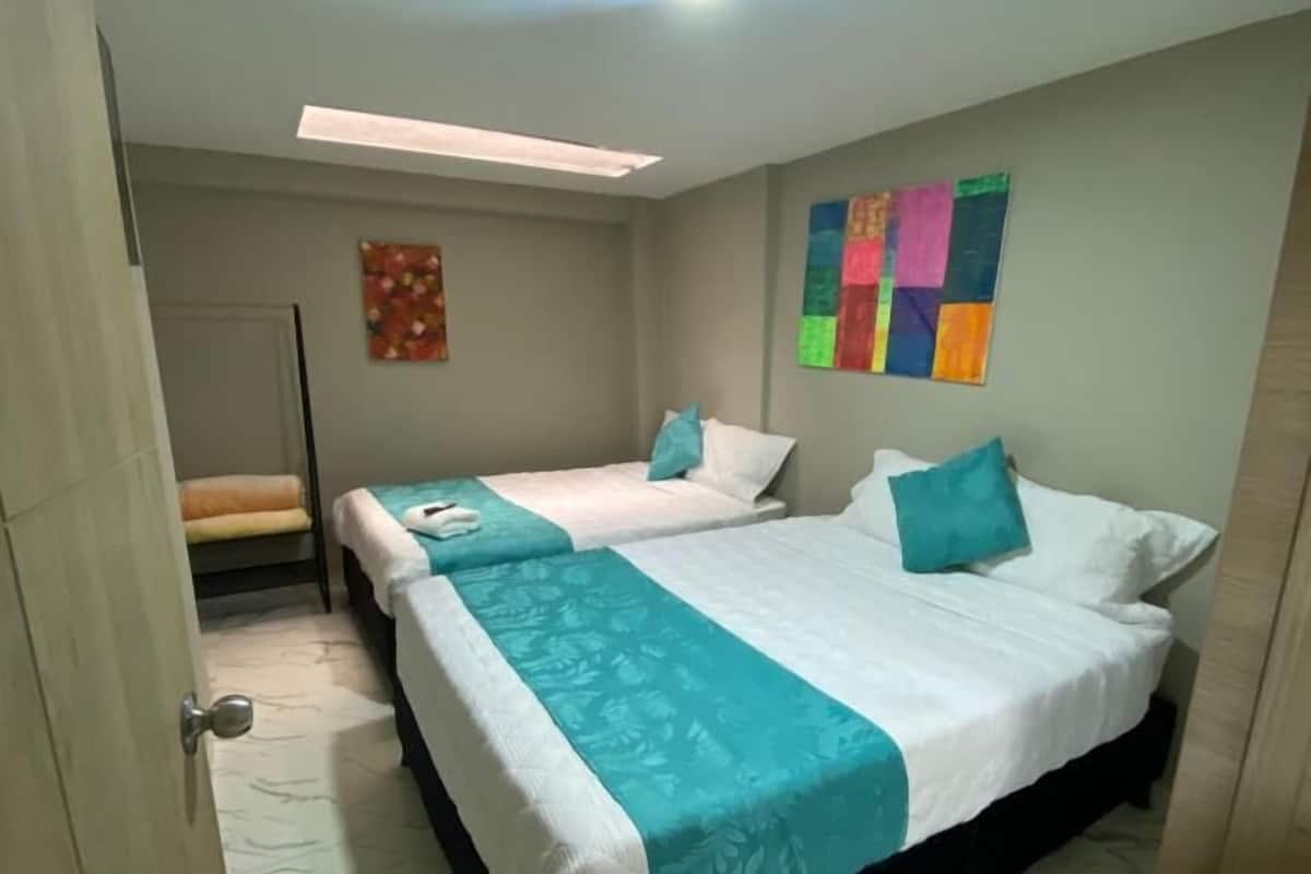 A hotel room with two beds, a small seating area, and a colorful artwork on the wall.