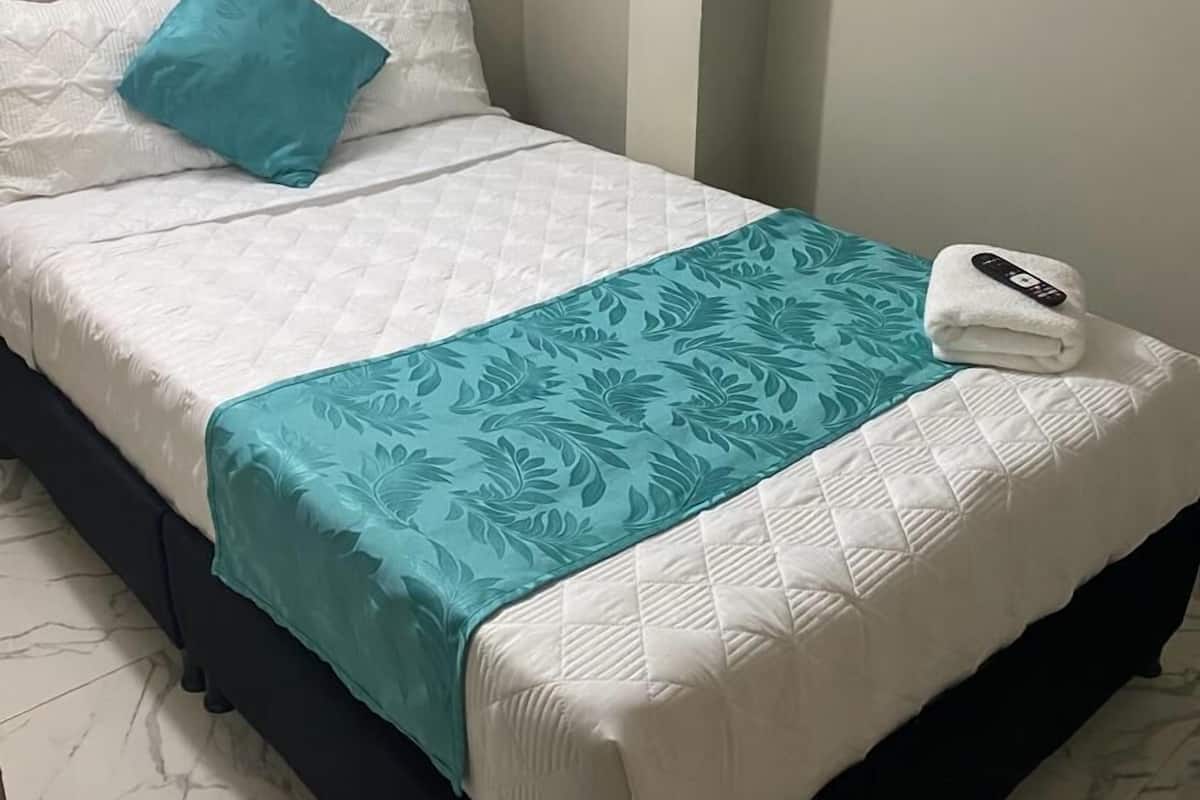 A neatly made bed with a white quilt, a teal floral bedspread, and a white towel with a remote control on it.