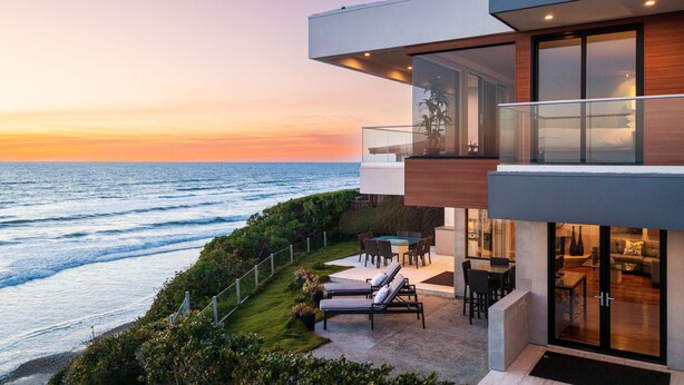 Een modern huis met een glazen balkon met uitzicht op de oceaan bij zonsondergang.