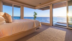 Een slaapkamer met een groot bed, uitzicht op de oceaan en een plant.
