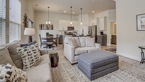 Un salon spacieux comprenant un canapé, un pouf et un coin repas avec une table et des chaises.