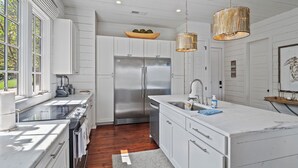 A modern kitchen with white cabinetry, a stainless steel refrigerator, and a large island with a sink. - Central Perk - pet friendly, luxury cabin feel,  coffee! (Crane Hill)