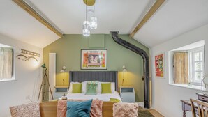 Quarto com cama, abajures, um pôster emoldurado, uma janela e uma cadeira de madeira.