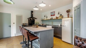 Cozinha moderna com ilha central, banquetas, geladeira e iluminação pendente.