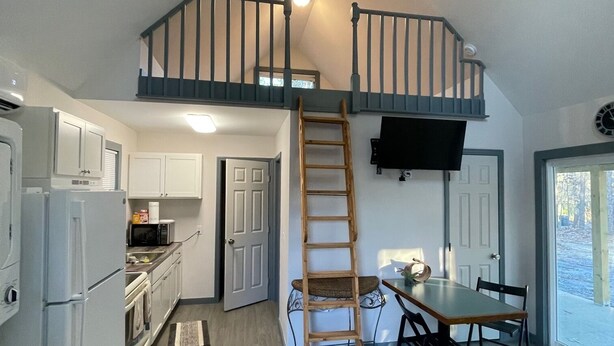 A loft-style kitchen with a wooden ladder leading to a mezzanine, a ceiling fan, and a dining area with a view of the outdoors. - Tiny House (not on water front) near lake martin, and boat ramp (Dadeville)