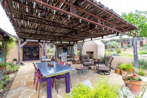 Un patio exterior con suelo de piedra, una parrilla y una zona de estar cubierta con sillas y una mesa.