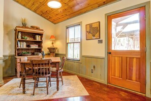 Un comedor de madera con una mesa, sillas, una estantería, una lámpara y una puerta con vistas al exterior.