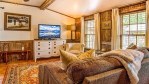 A cozy living room with a television, wooden furniture, and a large window with curtains. - Mucho Gusto in Bandera (Bandera)