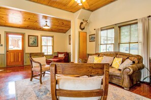 A cozy living room with wooden furniture, a fireplace, and a large window with blinds. - Mucho Gusto in Bandera (Bandera)