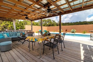 Un patio techado al aire libre con piscina, terraza de madera y mobiliario exterior.