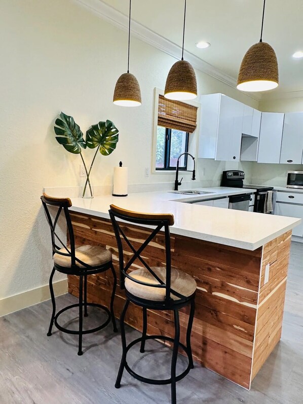 A kitchen with a wooden island, two bar stools, pendant lights, a large plant, and white cabinets.