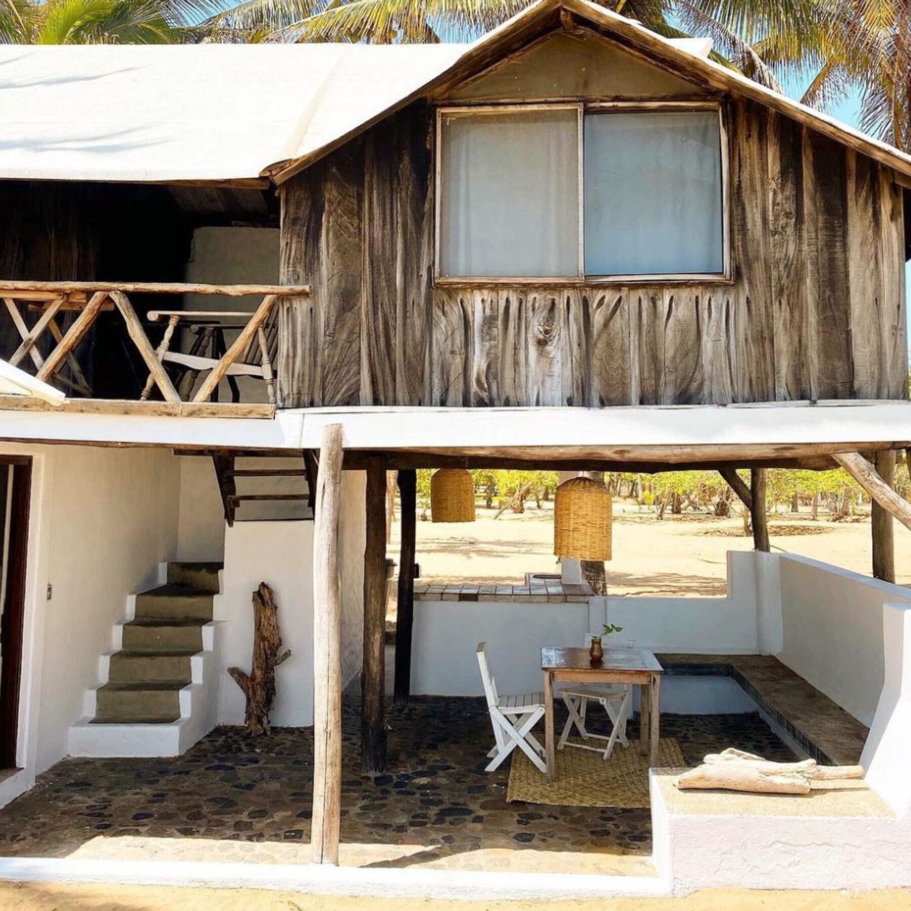 A rustic wooden building with a balcony, a staircase leading to an upper level, and a small outdoor seating area with a table and chairs.