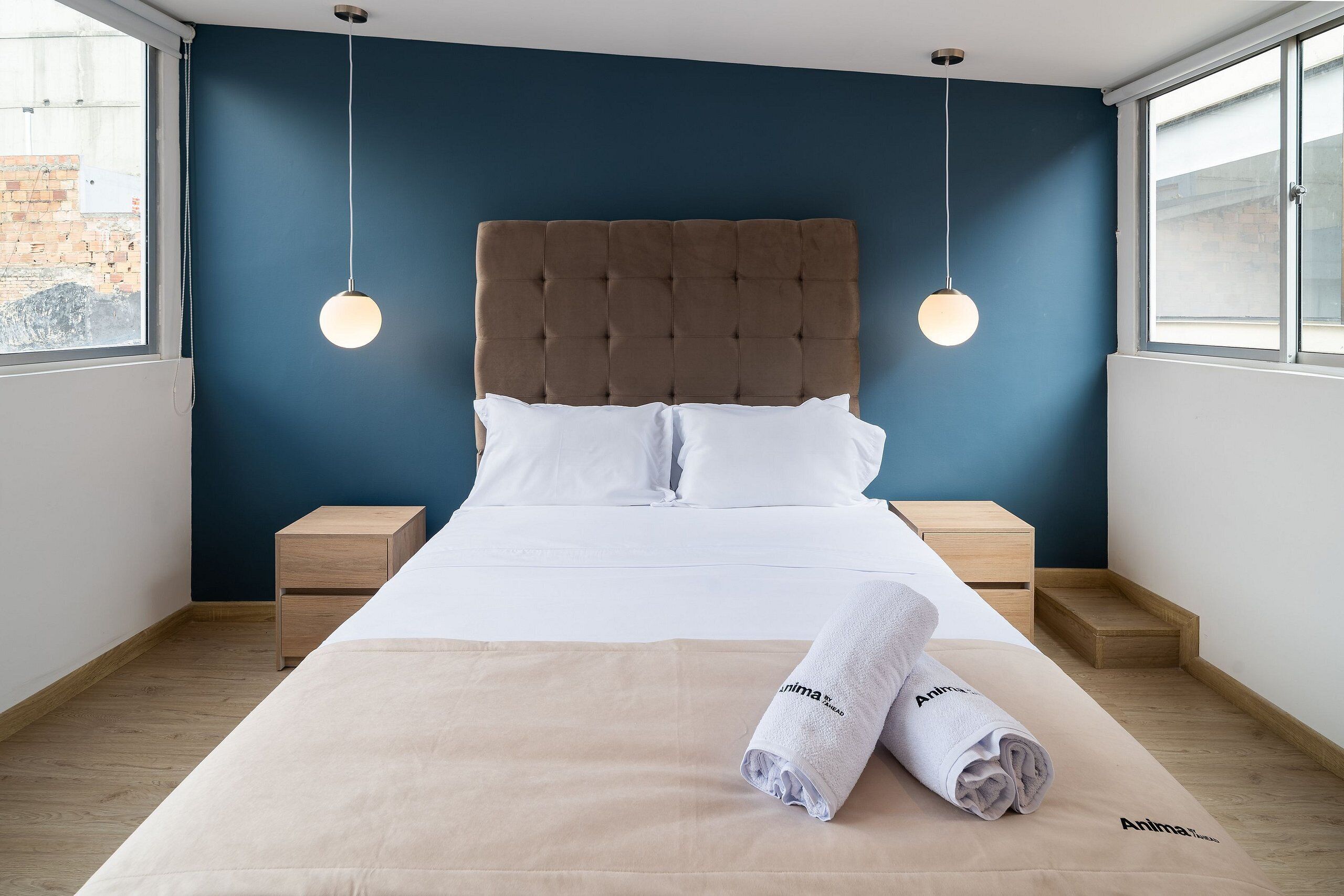A neatly made bed with a brown headboard, white bedding, and two bedside tables.