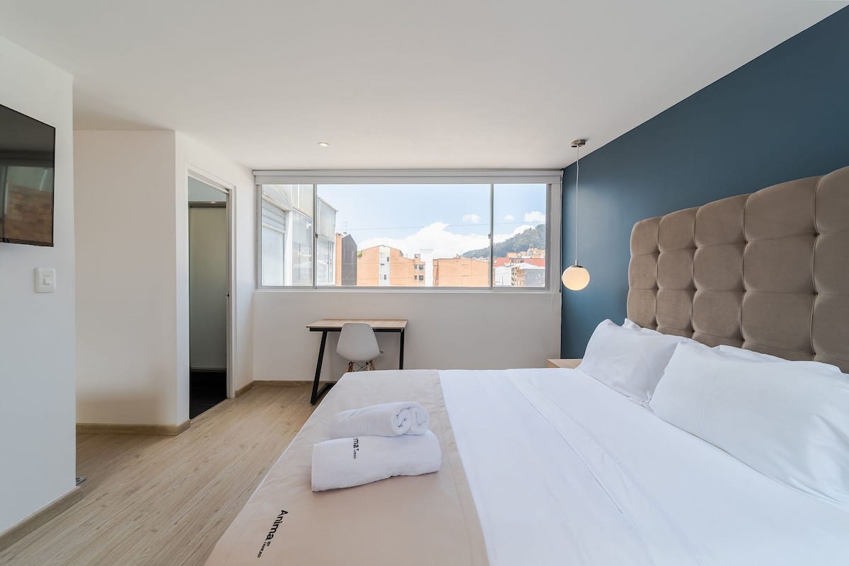 Une chambre d’hôtel moderne avec un grand lit, un bureau et une vue sur les immeubles par la fenêtre.