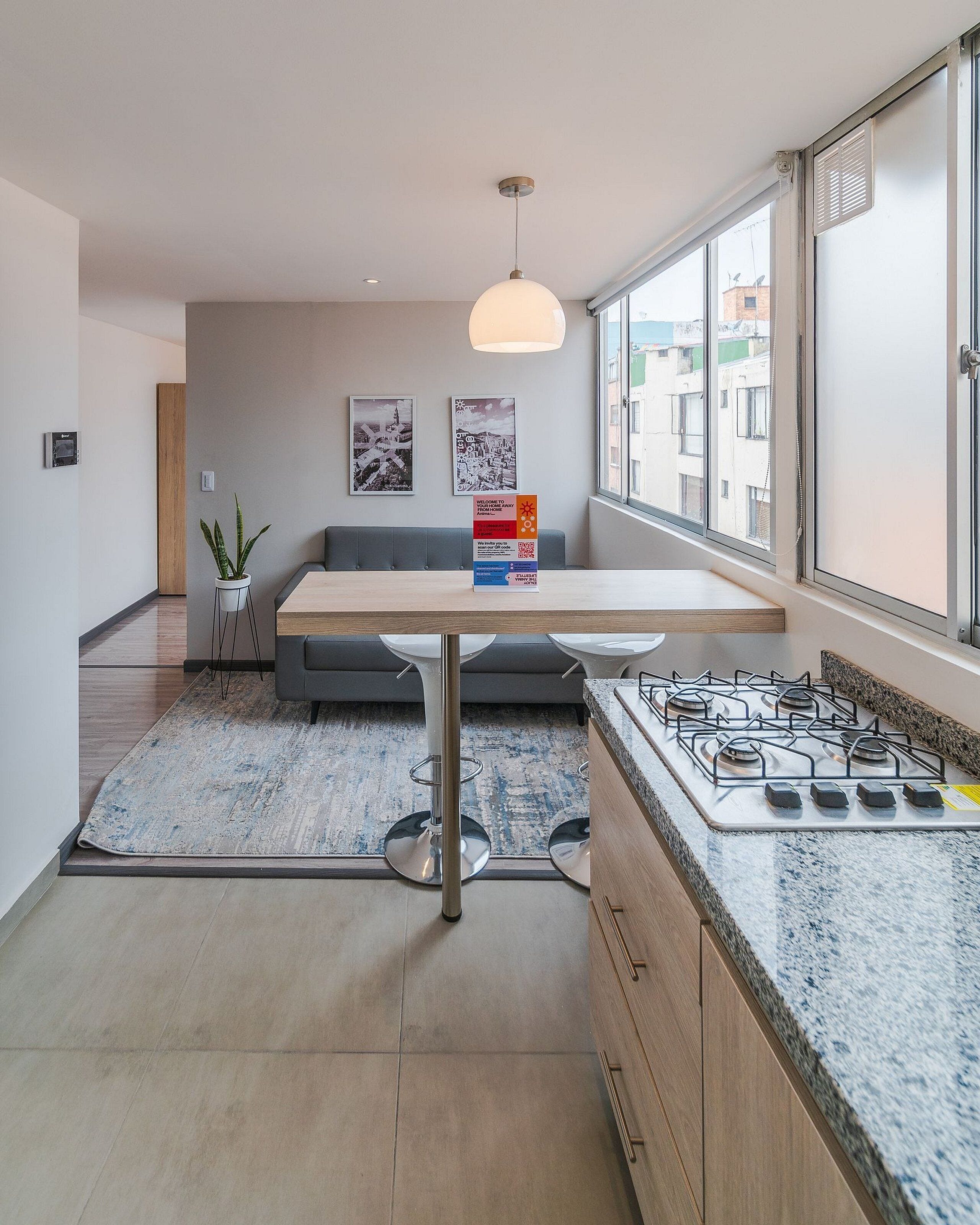 A modern kitchen with a built-in gas stove, a wooden dining table, and a grey sofa in the background.