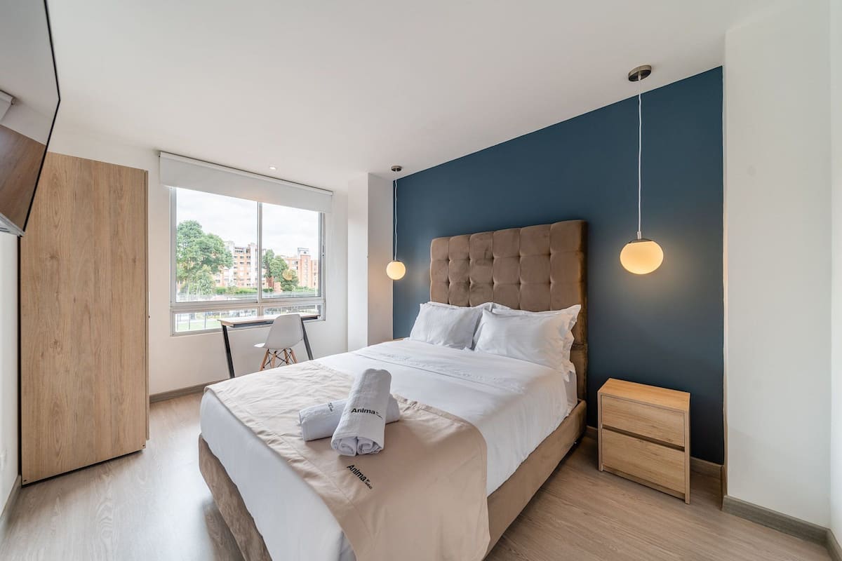 Une chambre d’hôtel moderne dotée d’un grand lit, d’une armoire en bois, d’un bureau avec une chaise et d’une fenêtre donnant sur la ville.