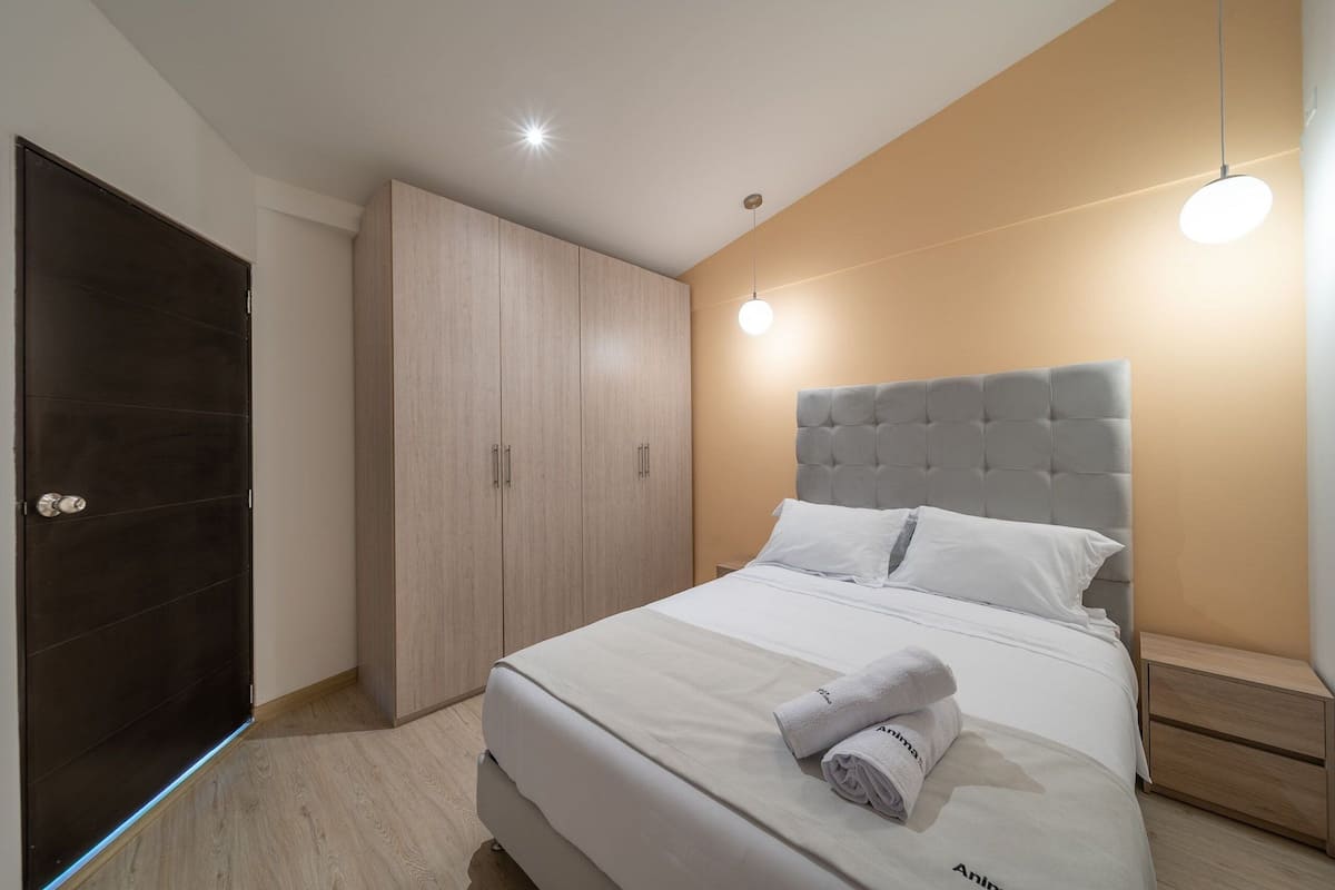 Une chambre à coucher moderne avec un grand lit, une tête de lit rembourrée de couleur grise et une armoire en bois.