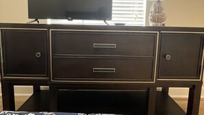 A bedroom with a TV on a dresser, a lamp, and a window with blinds.