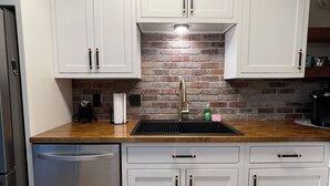 A kitchen with white cabinets, a brick backsplash, a stainless steel dishwasher, and a black sink.
