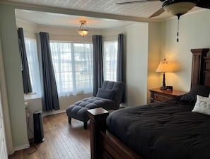 A bedroom with a bed, a chair, a lamp, and a window with curtains. - 2 min from rt 66- hot tub-firepit-bocceball-bbq (Williams)