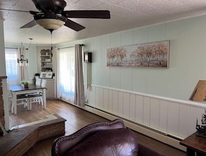 A living room with a brown leather chair, a ceiling fan, a dining area with a table and chairs, and a painting on the wall. - 2 min from rt 66- hot tub-firepit-bocceball-bbq (Williams)