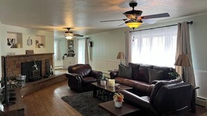 A living room with a fireplace, leather sofas, a coffee table, and a ceiling fan. - 2 min from rt 66- hot tub-firepit-bocceball-bbq (Williams)