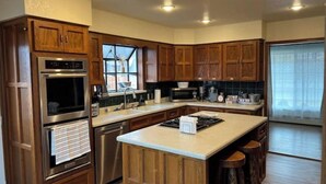 A kitchen with wooden cabinets, stainless steel appliances, and a large island with stools. - 2 min from rt 66- hot tub-firepit-bocceball-bbq (Williams)