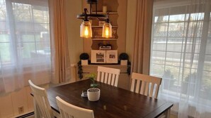 A dining area with a dark wooden table, white chairs, and a hanging light fixture. - 2 min from rt 66- hot tub-firepit-bocceball-bbq (Williams)