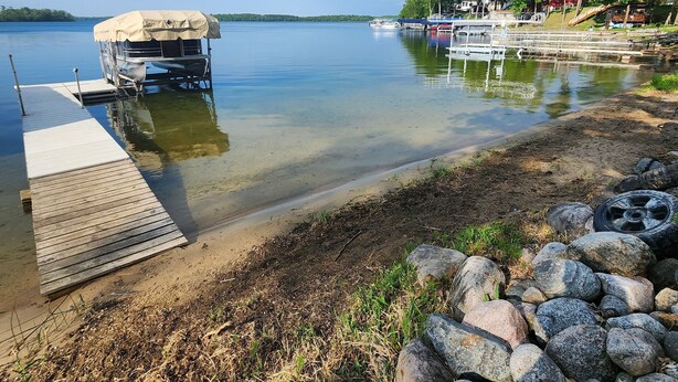 A lakeside dock with a covered boat, calm water, and a rocky shoreline. - Lake Front, Pontoon, Bunk House (Rochert)