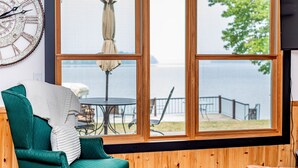 A room with a large window overlooking a body of water, a green chair, and a rustic wooden wall. - Lake Front, Pontoon, Bunk House (Rochert)