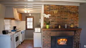 A kitchen with a brick fireplace, white appliances, and a window with a view. - Les Rosiers - ONJON - Gîte (ONJON)