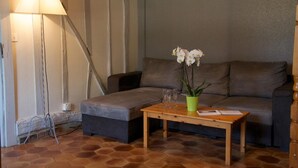 A living room with a sofa, a wooden coffee table with a vase of flowers, and a floor lamp. - Les Rosiers - ONJON - Gîte (ONJON)